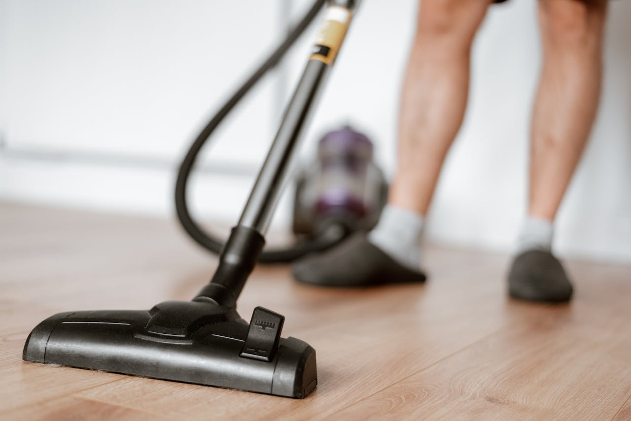 services-01 Crop anonymous male in slippers washing floor with vacuum cleaner in flat during household routine